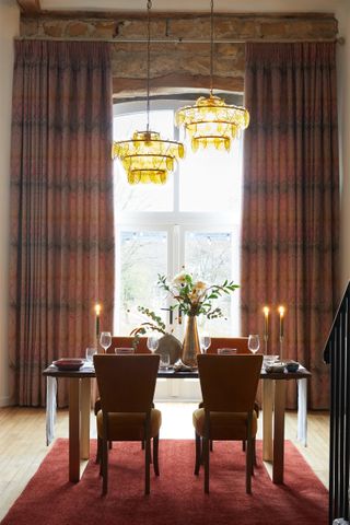 dining room with two metallic vases with flowers, candlesticks, two pendant lights, damask style drapes, exposed brick wall