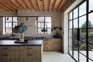 a rustic reclaimed kitchen in a minimalist house with crittall doors and exposed roof rafters