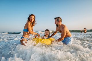parents playing with child in an inflatable in the sea waves