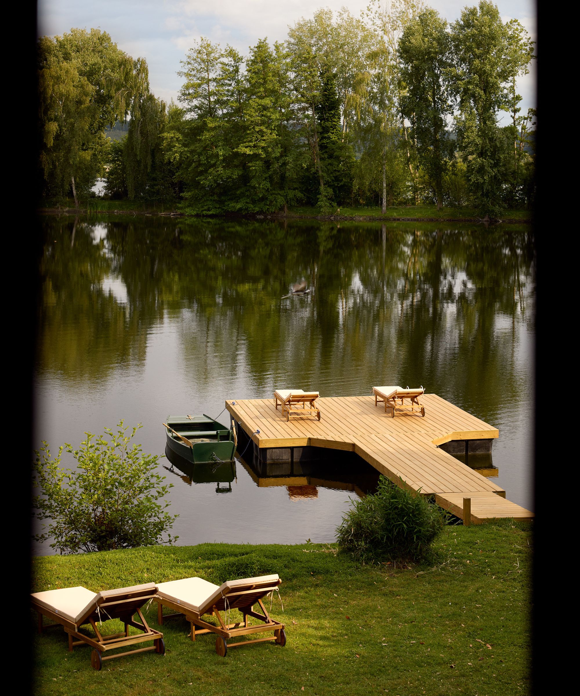 a lake in France with a wooden jetty suspended in the water with loungers and a small green fishermans boat