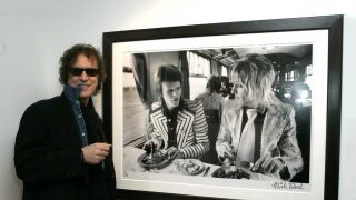 Mick Rock next to a portrait of David Bowie and Mick Ronson 