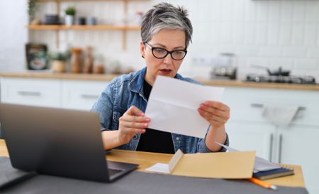 Shocked woman holding big Medicare bill at home.
