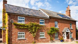 large brick cottage style property with tiled roof and two solar panels on roof