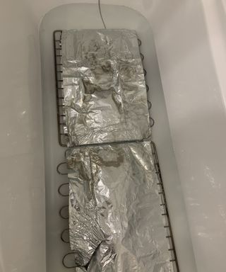 oven racks being cleaned with tiktok hack using foil and dishwasher tablet