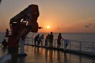 The crew on the research vessel looking out at an ocean sunset.