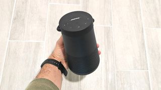 Bose speaker held in hand against with a tiled floor in the background