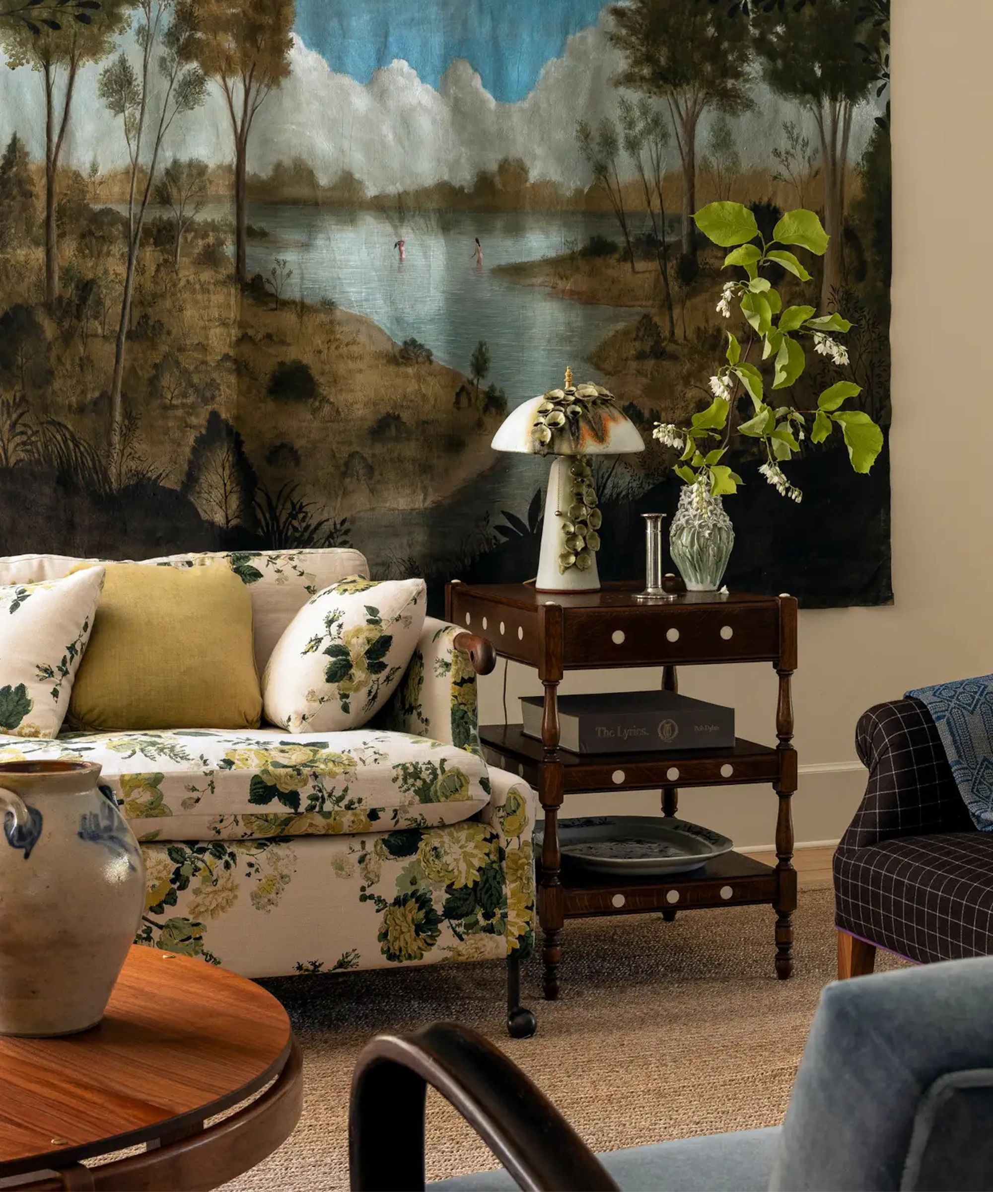 old meets new cozy living room with a large wall-hung tapestry, a neutral and yellow floral sofa with antique wooden furniture and ceramics