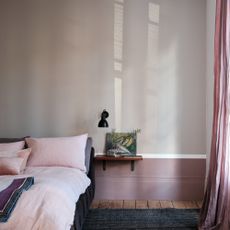 A bedroom with a the top half of the wall painted in Farrow & Ball's Elephant's Breath with pink bed linen and curtains on the window