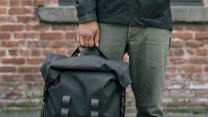Man stood holding the Chrome Industries Urban Ex Rolltop 2.0 backpack