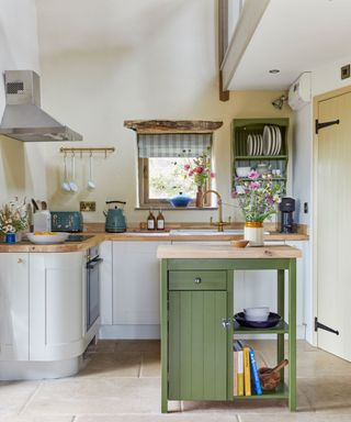 kitchen area with small green kitchen island, wooden beam above window and a cream shaker style kitchen with wooden worktop