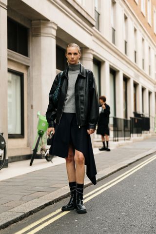 woman wearing leather jacket, gray turtleneck, black skirt, and black boots