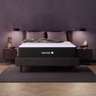 A Nectar Premier Mattress on a bed with pillows against a purple wall.