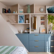A pink-painted bedroom with built-in shelves and fluted drawers in blue