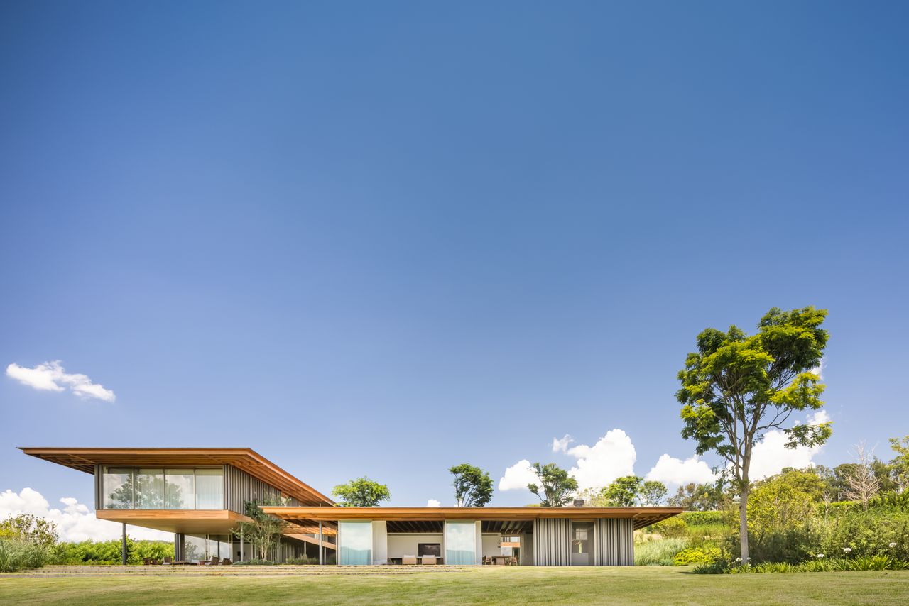 The YJD House, a complex with wood roof, large glass windows surrounded by green nature. 