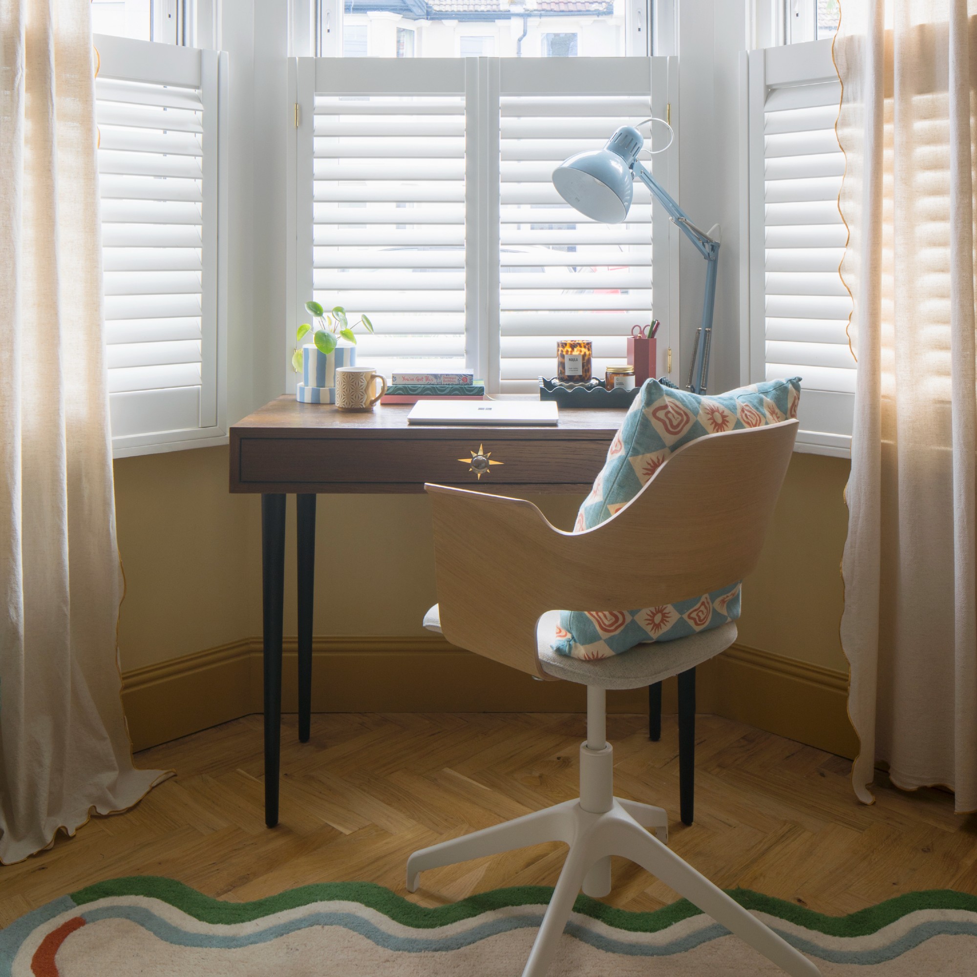 A home office in a spare bedroom by the window with a rotating office chair and a wavy-edge rug