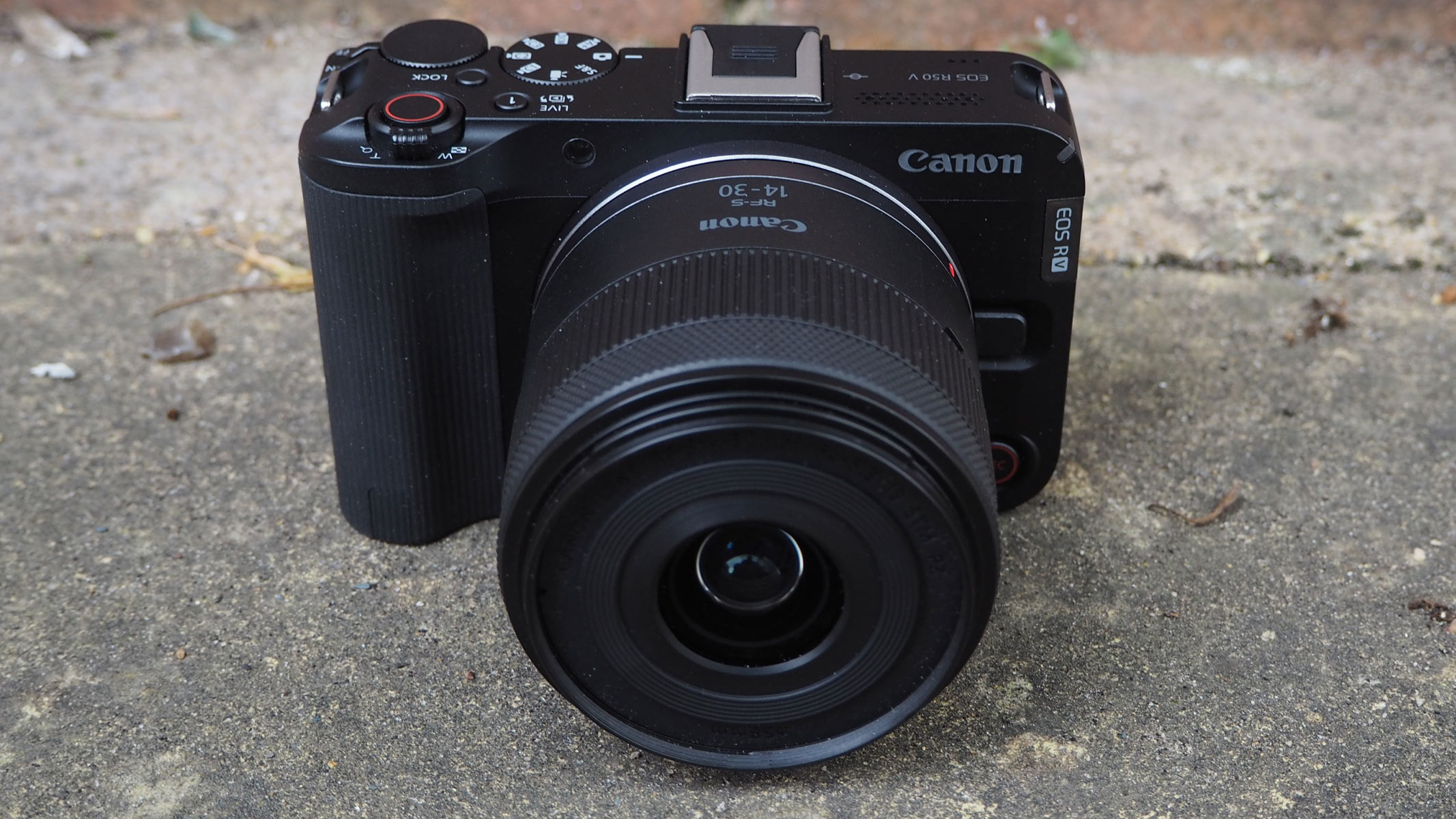 The Canon EOS R50 V with lens on concrete floor.
