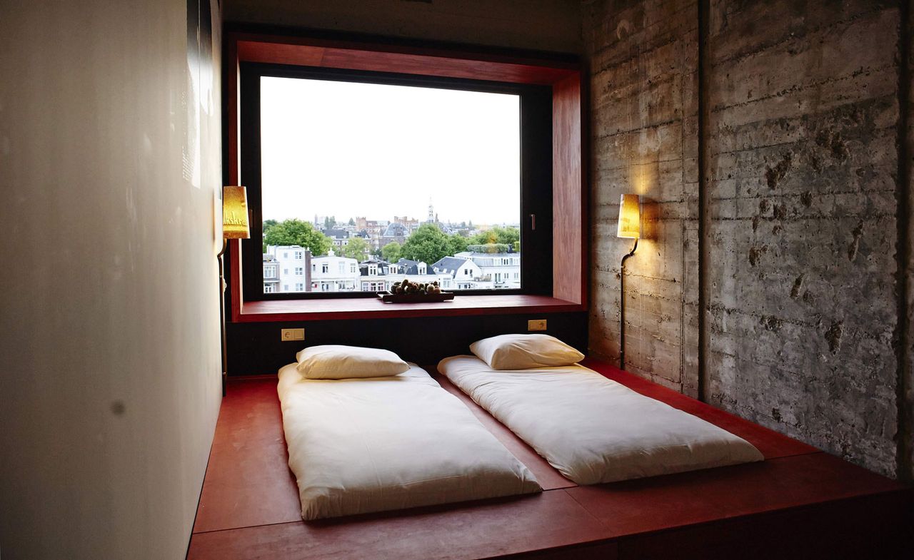 Volkshotel room with 2 single mattresses on wooden platform, exposed brick walls and large window