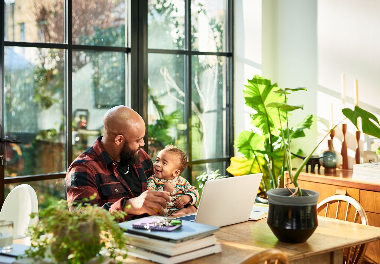 father smiling face to face with baby son in front of laptop in home office