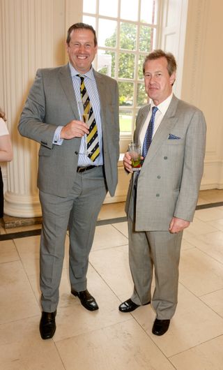 Lord Ivar Mountbatten stands on the right hand side and wears a light gray suit and holds a drink in his hand