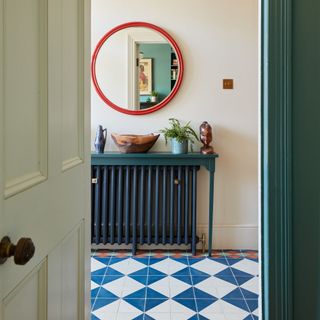 Hallway with blue and white tiled floor, a red round mirror on the wall and a blue radiator