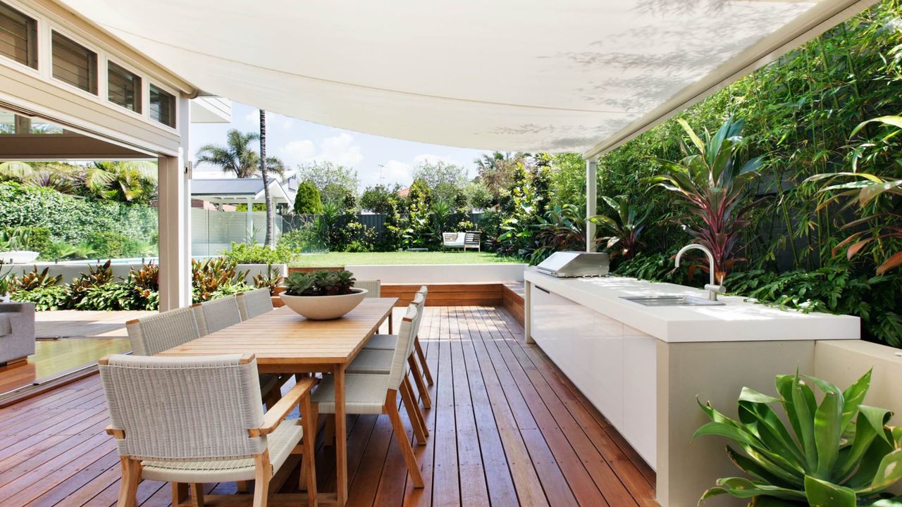 An outdoor kitchen with deck, dining area, and fabric shade