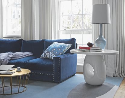 living room with blue sofa and small white coffee table styled with a lamp and books