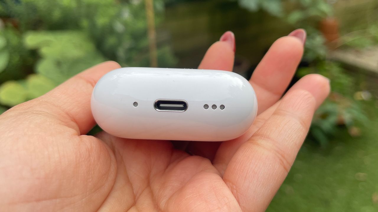 The Apple AirPods 4 case held to show the charging port and speaker on the bottom.