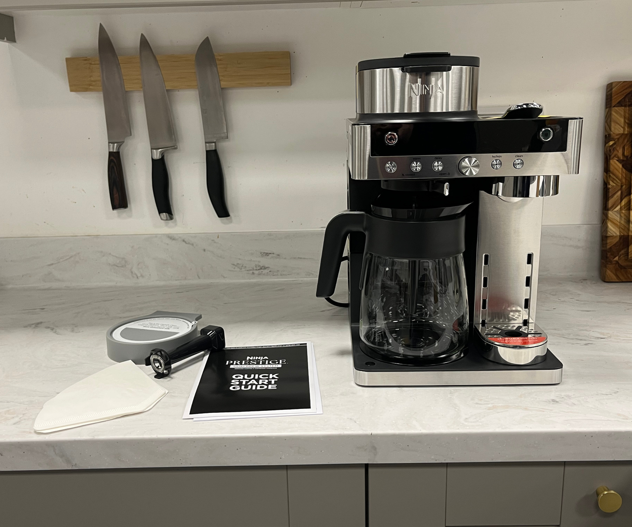 Ninja Prestige DualBrew System espresso and drip coffee maker on a white countertop, beside the instruction manual.