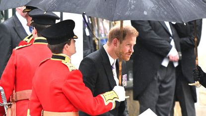 Prince Harry walking under an umbrella