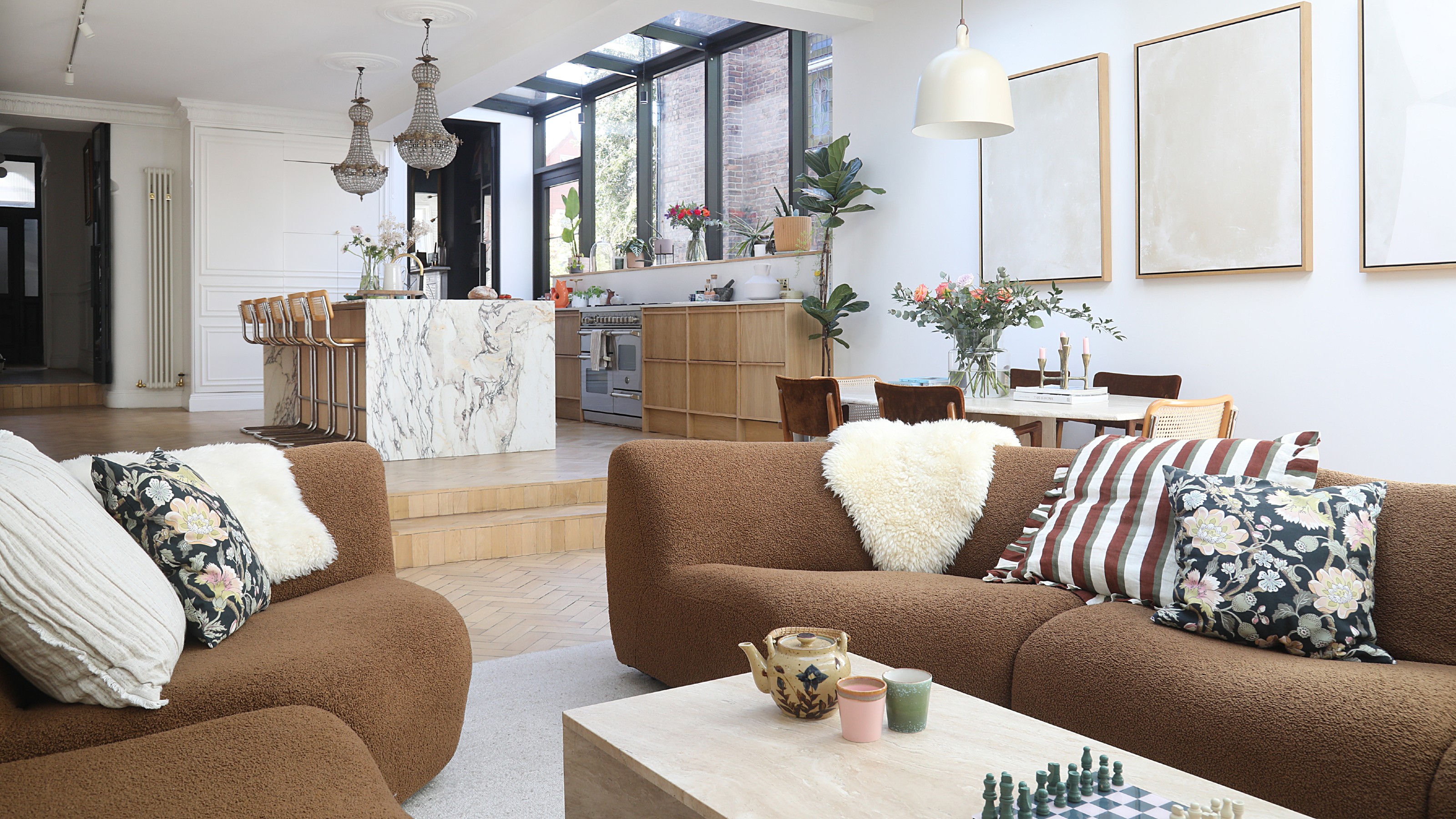 An open-plan living room with a brown modular sofa and a kitchen in the background