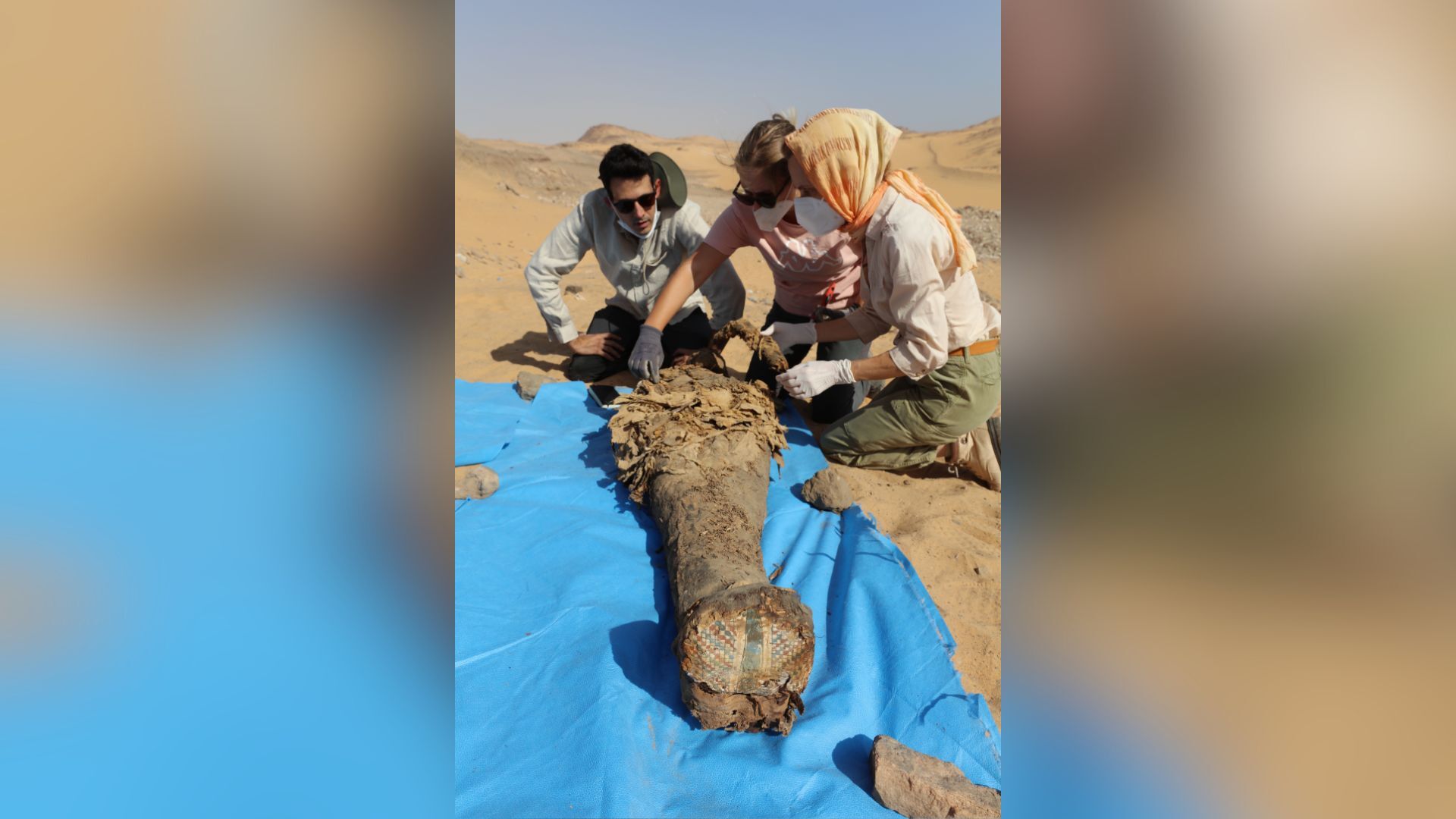 Three archaeologists observing an Aswan mummy laid on the ground