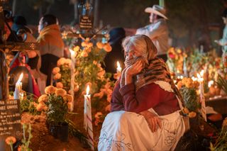 The Día de los Muertos in Oaxaca, Mexico is a deeply spiritual and culturally rich celebration of life and death. The elderly woman sits contemplatively among the graves adorned with bright orange marigolds, candles, and personal mementos. Her expression reflects a mixture of sorrow and peace, perhaps as she communes with the spirits of her loved ones. The warm glow of candlelight illuminates the scene, creating a sacred and intimate atmosphere