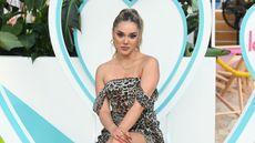 Cely Vazquez in a leopard print off the shoulder dress sitting in front of a blue and white heart