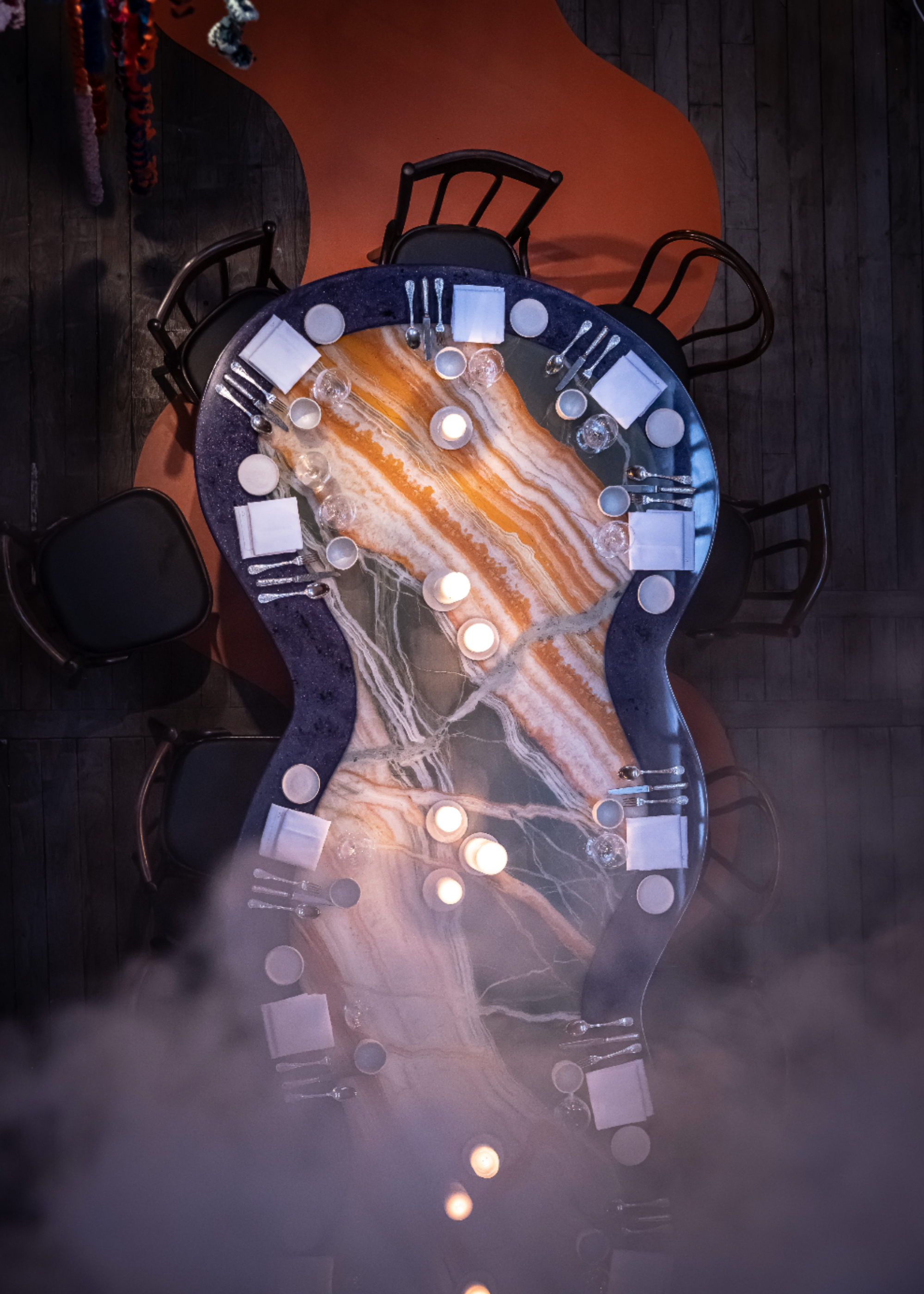 a curbed black rimmed marble dining table set for a meal with black dining chairs all around and smoke covering half of the table