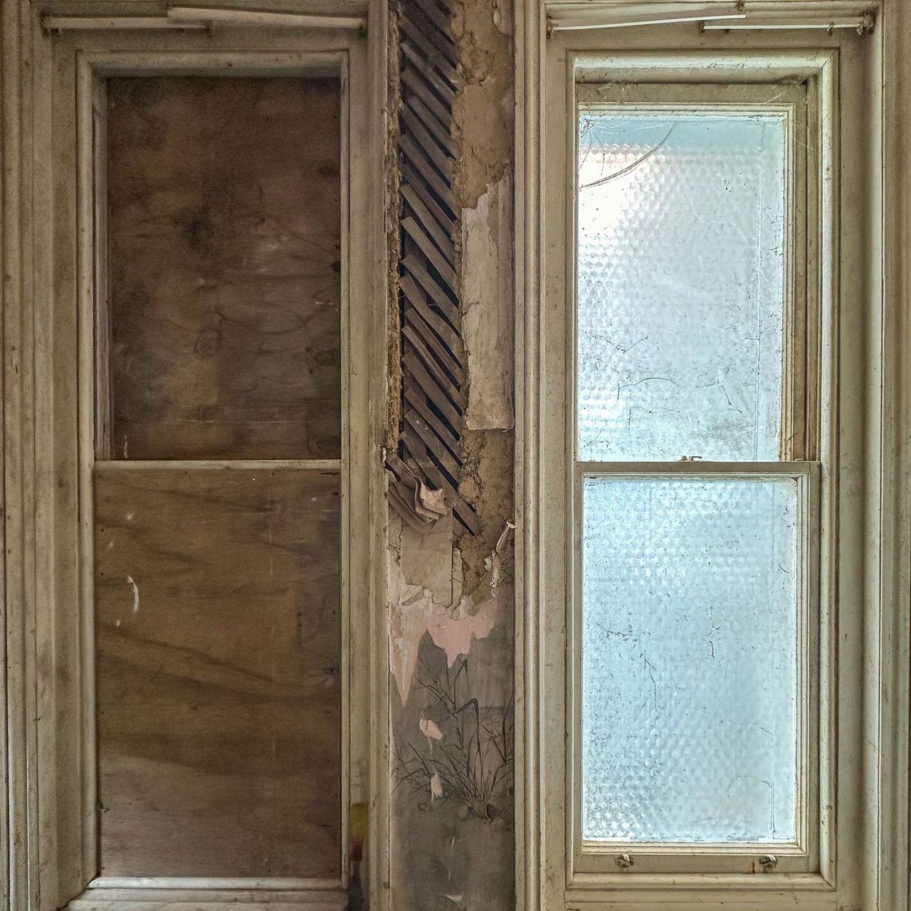 Interior view of two windows in room mid-renovation, one boarded up