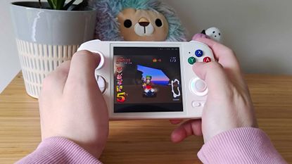 Hands holding Anbernic RG Cube with Crash Team Racing gameplay on screen.