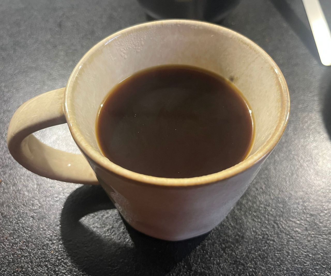 A beige cup of dark coffee on a black counter.