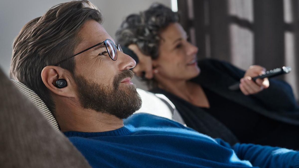 A man on a sofa listening to a pair of Sennheiser TV Clear.