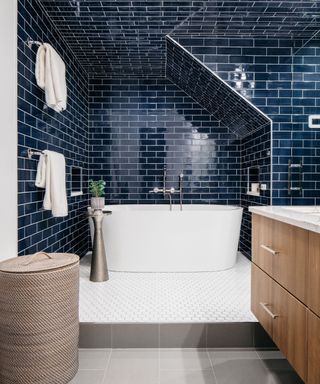 Bathroom with raised bathtub area, white floor tiles and tub, dark blue wall and floor tiles, wood vanity