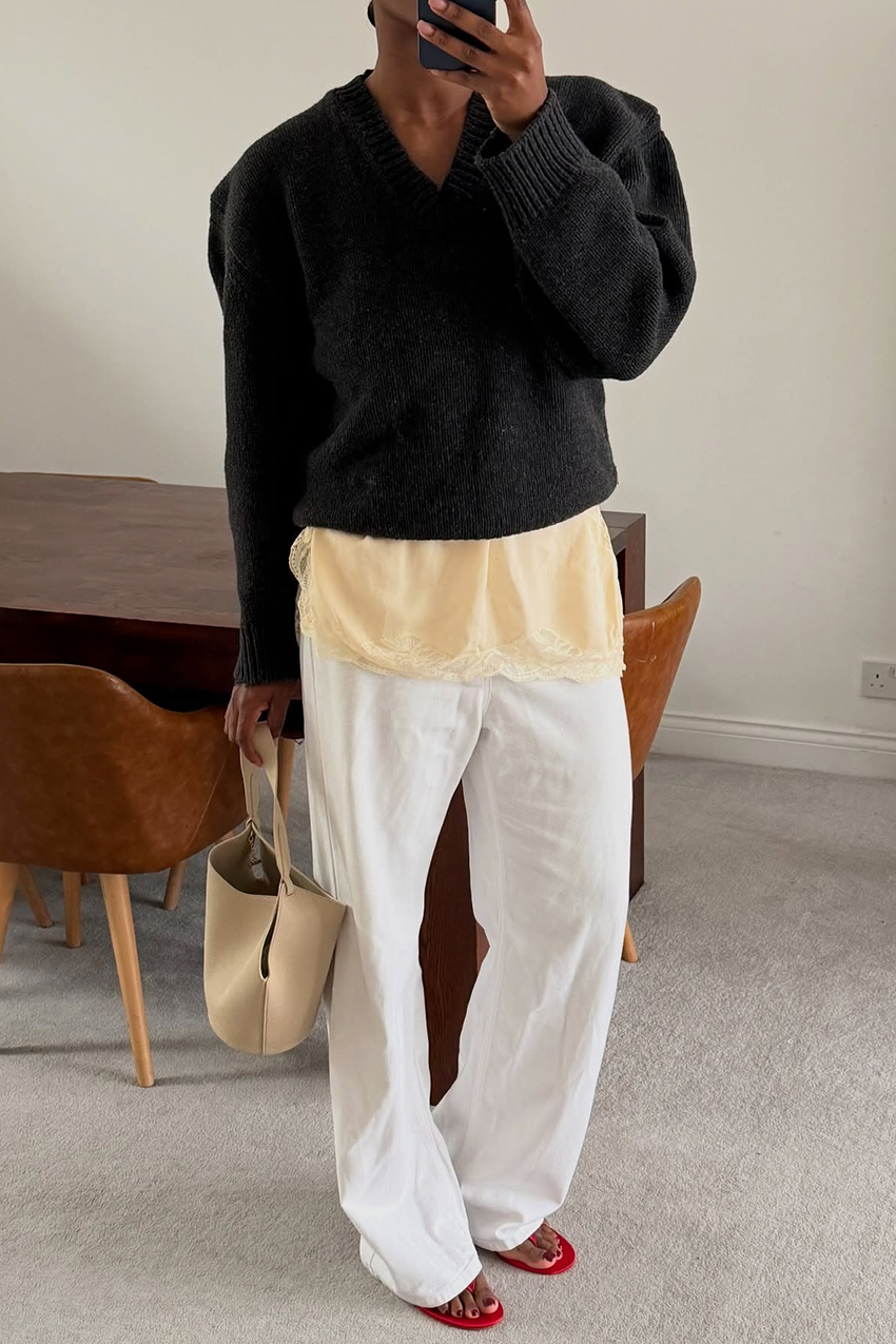 a woman wearing a black V-neck, lace trim satin top, white jeans, and red sandals