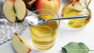 Glass of apple cider vinegar on a tabletop close up with spoon on top
