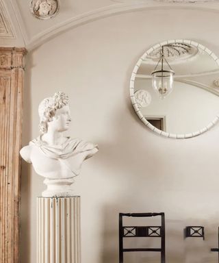 Neutral room with round mirror a sculpture of a head on a pedestal