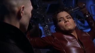 Halle Berry in a red leather jacket looking in pain with a man looking at her.