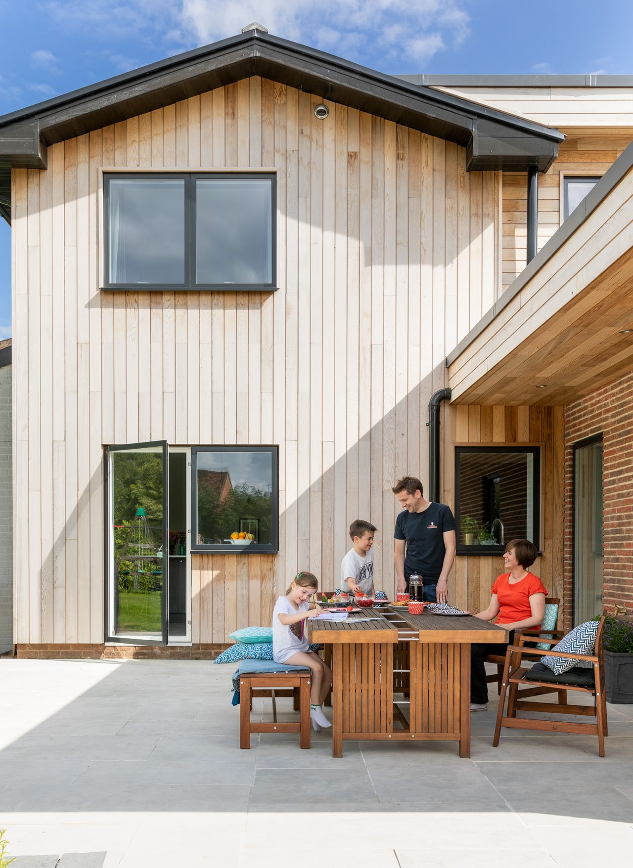 Overhangs are an important element in the design, while a new patio space to the side elevation (right) uses similar porcelain to the interiors in neutral tones (from Bradstone).