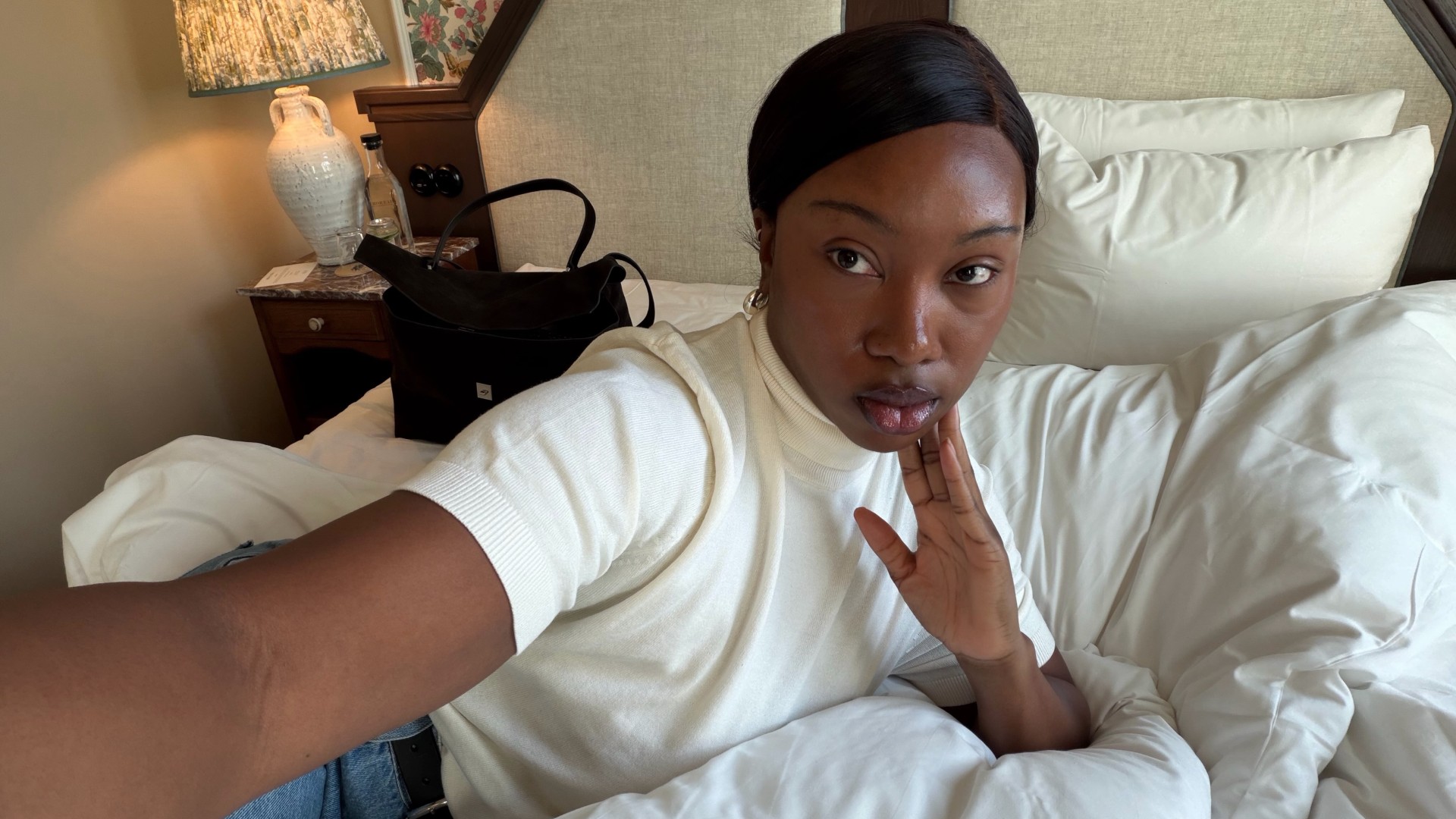 A woman taking a selfie from bed in a white T-shirt and jeans.