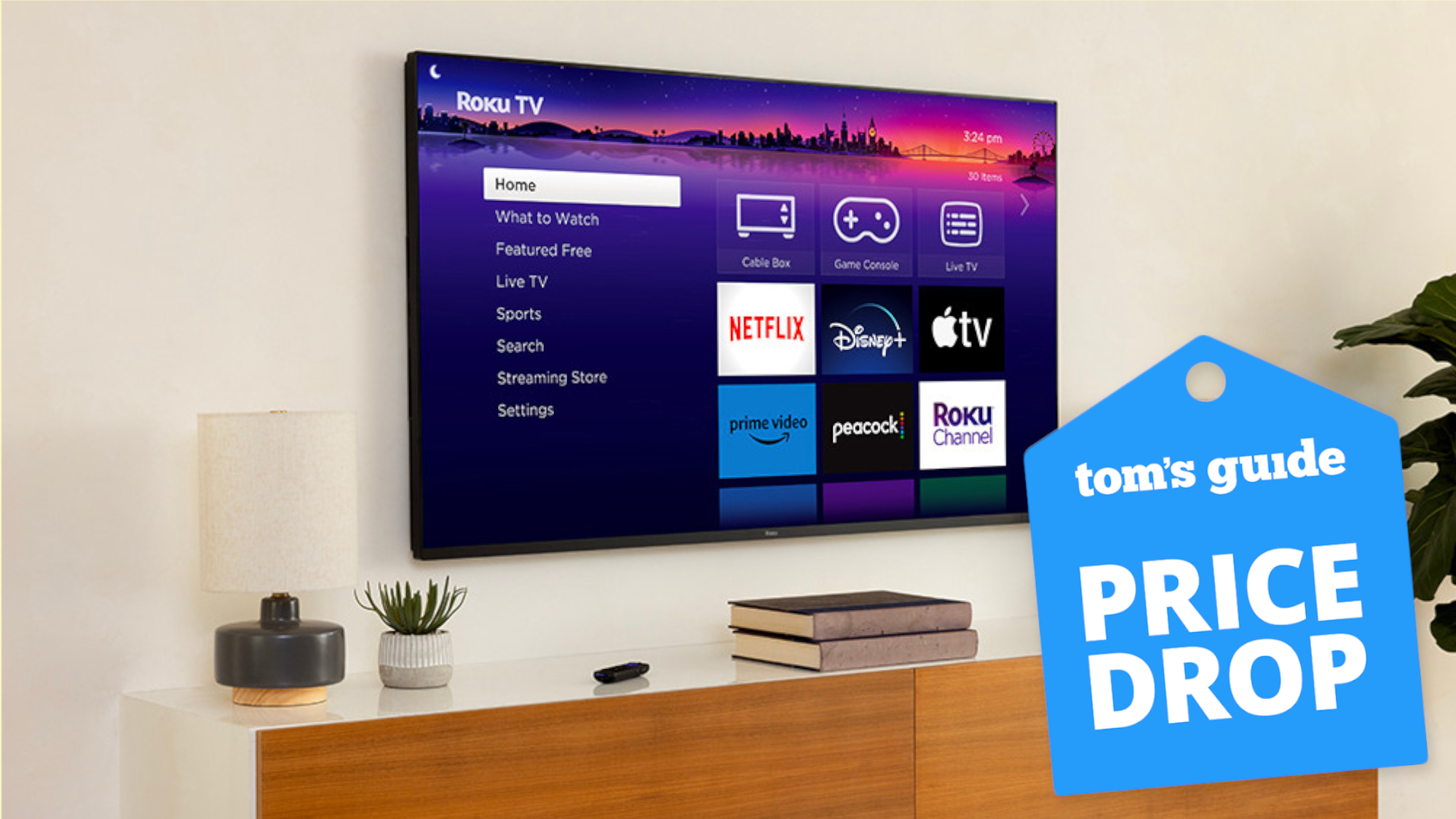 A wall-mounted Roku Pro Series TV displaying the Roku OS home screen. On the right-hand side of the image is a blue-colored badge that reads: Tom's Guide - Price Drop