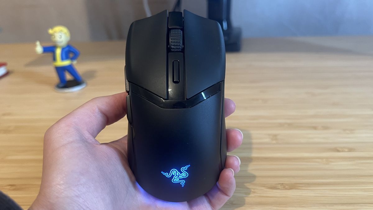 Razer Cobra Hyperspeed gaming mouse in reviewer's hand in front of wooden desk