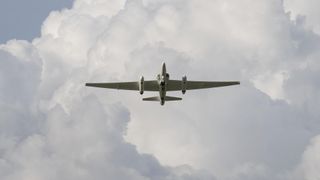 a plane with a large wingspan flies under cloudy skies