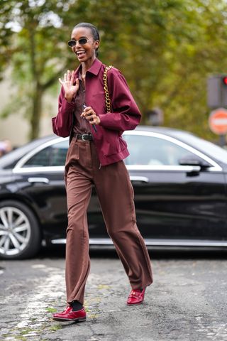 A model wears black sunglasses, dark red oversized jacket, dark brown buttoned up shirt, dark brown loose pants, shiny dark red loafer moccasin leather shoes, outside Chloe, during the Paris Fashion Week Spring/Summer 2025 on September 26, 2024 in Paris, France