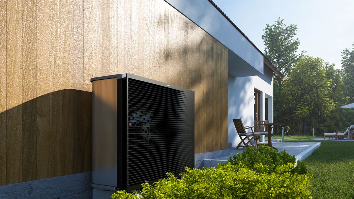 A grey and black Daikin heat pump up against a wooden exterior of a house